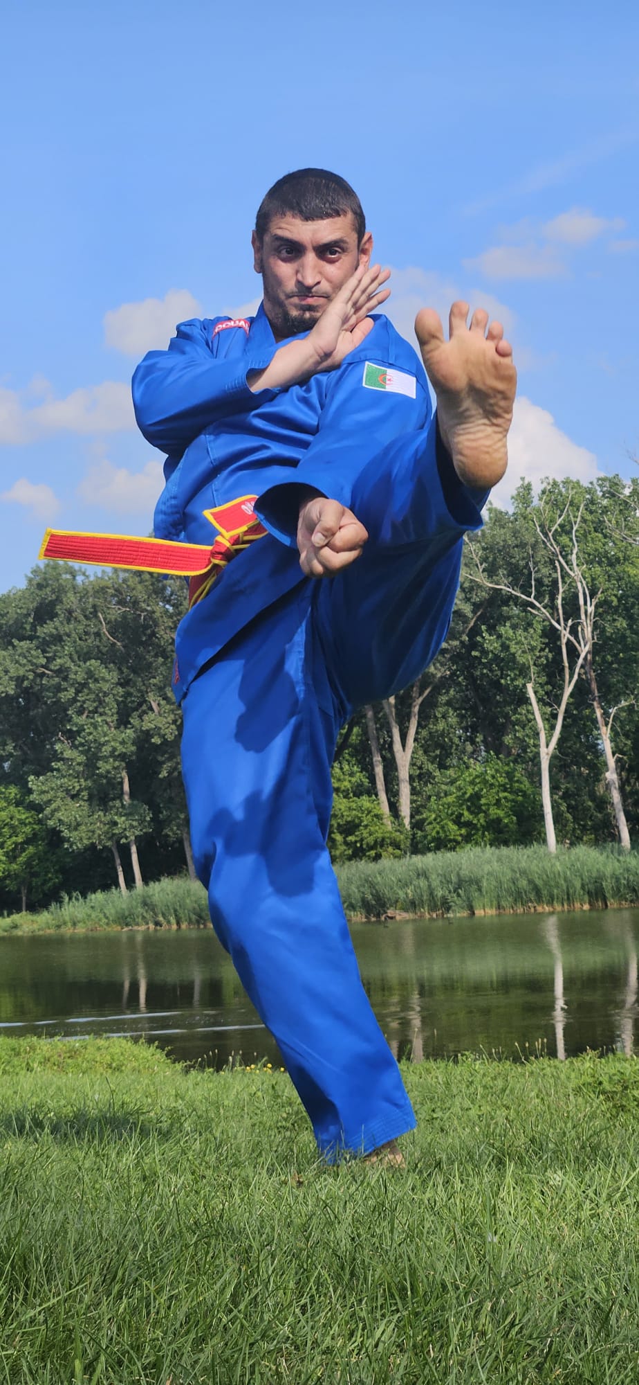 Master Guendouzi throwing a high front kick by the lake in his blue Vovinam gi