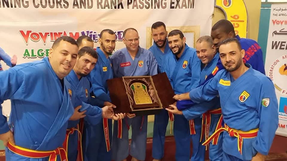Instructor team holding the framed rank-passing-exam plaque at the African Federation